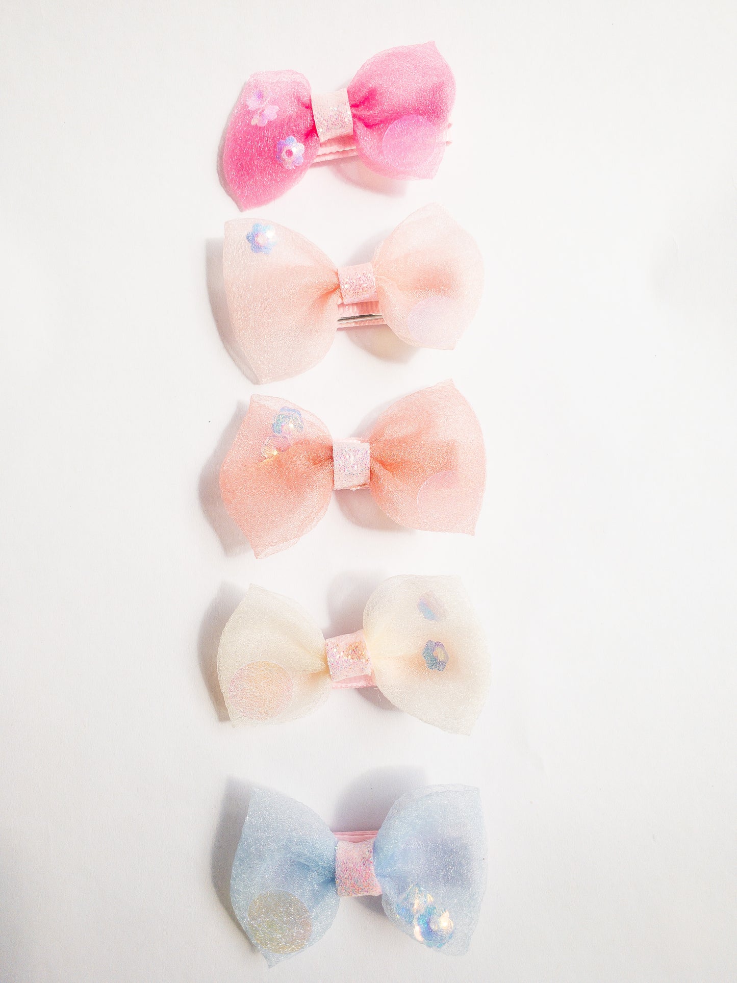 Pretty and fun, these sheer confetti shimmer bows are sure to brighten up any look. A set of 5 alligator fabric wrapped hair clips, each bow has a glitter center and is filled with little flowers and iridescent dots.