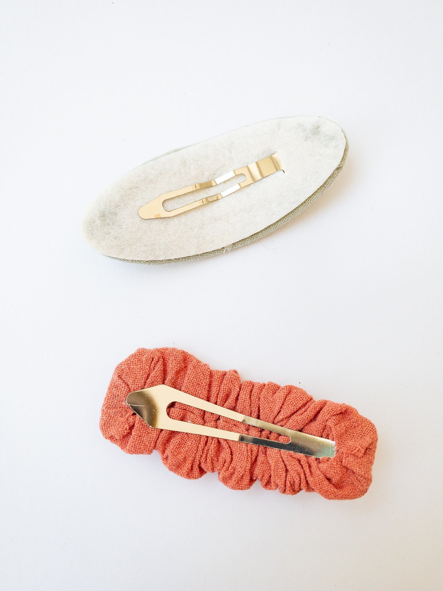 A set of two beautiful fabric wrapped snap clip barrettes. One oval barrette with an embroidered flower and one rectangular ruffled fabric barrette.