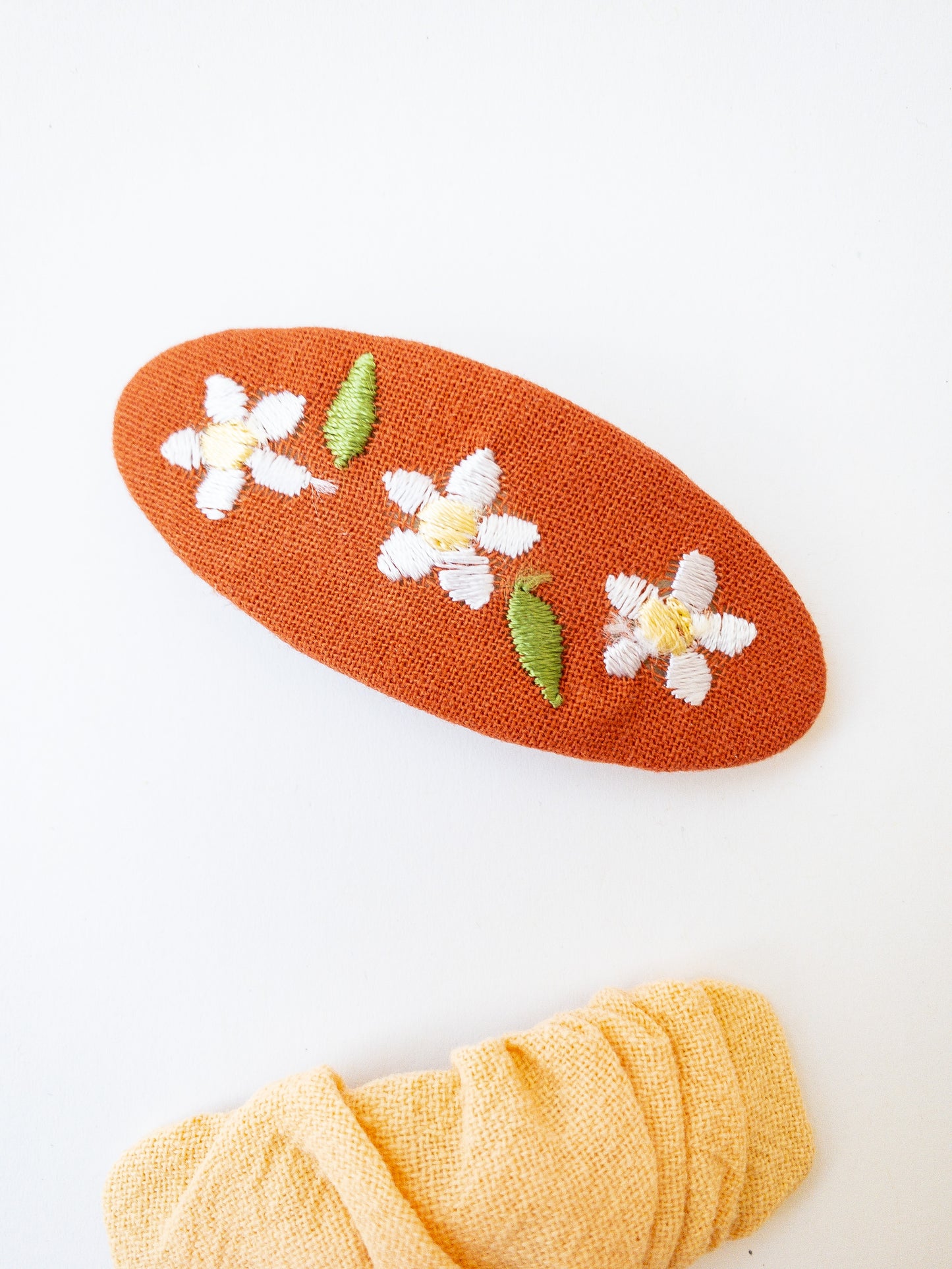 A set of two beautiful fabric wrapped snap clip barrettes. One oval barrette with an embroidered flower and one rectangular ruffled fabric barrette.