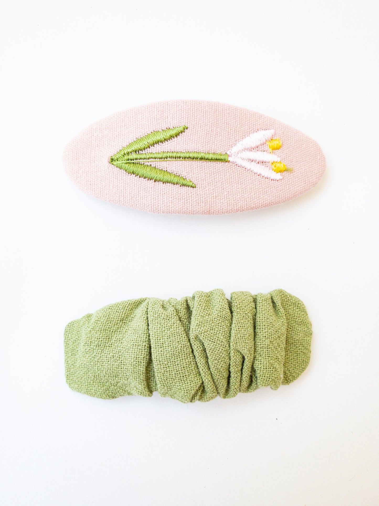 A set of two beautiful fabric wrapped snap clip barrettes. One oval barrette with an embroidered flower and one rectangular ruffled fabric barrette.