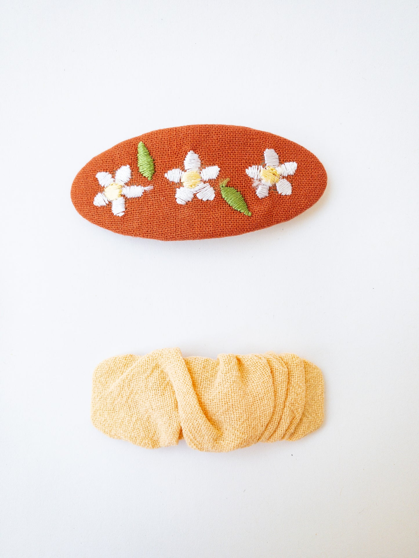 A set of two beautiful fabric wrapped snap clip barrettes. One oval barrette with an embroidered flower and one rectangular ruffled fabric barrette.