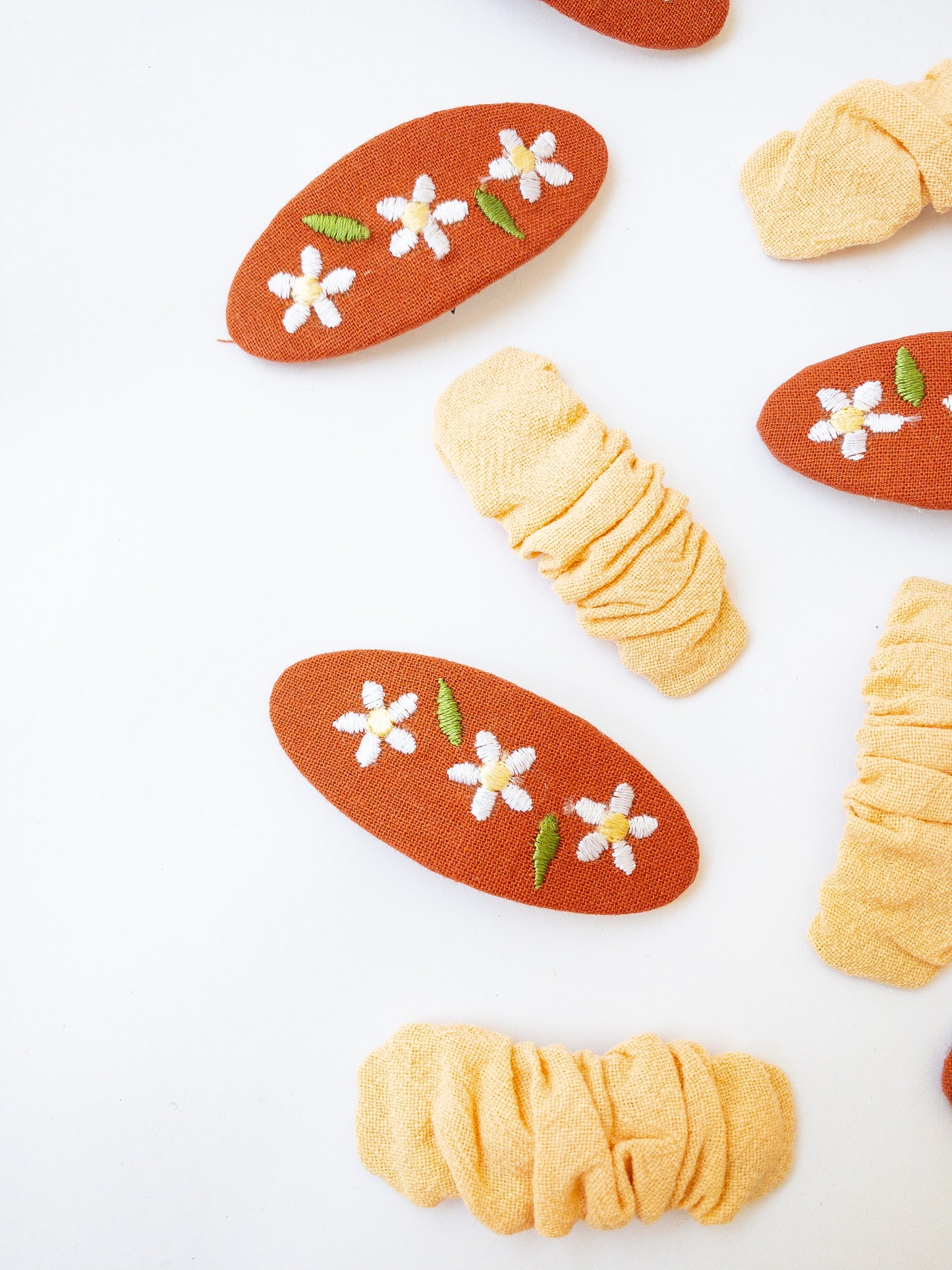 A set of two beautiful fabric wrapped snap clip barrettes. One oval barrette with an embroidered flower and one rectangular ruffled fabric barrette.
