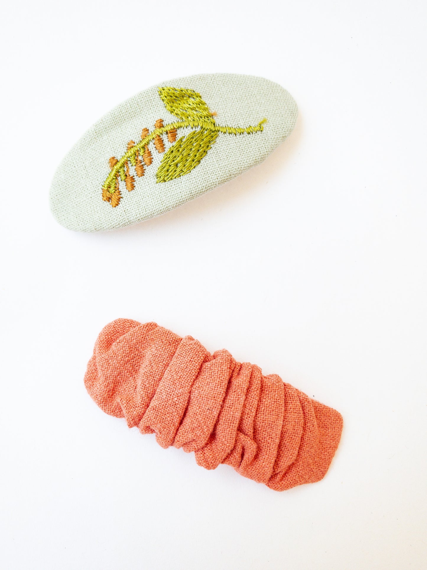 A set of two beautiful fabric wrapped snap clip barrettes. One oval barrette with an embroidered flower and one rectangular ruffled fabric barrette.