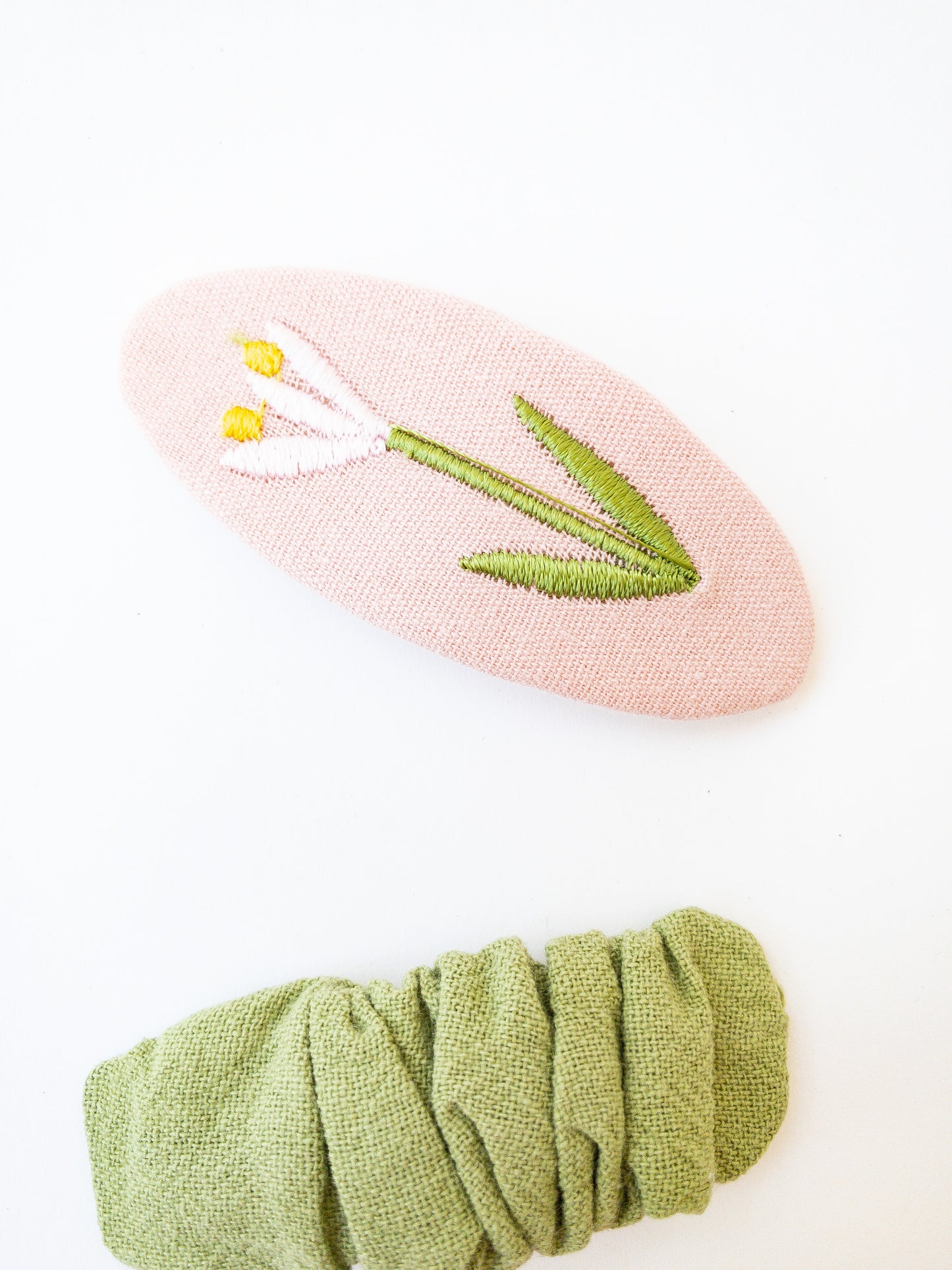 A set of two beautiful fabric wrapped snap clip barrettes. One oval barrette with an embroidered flower and one rectangular ruffled fabric barrette.