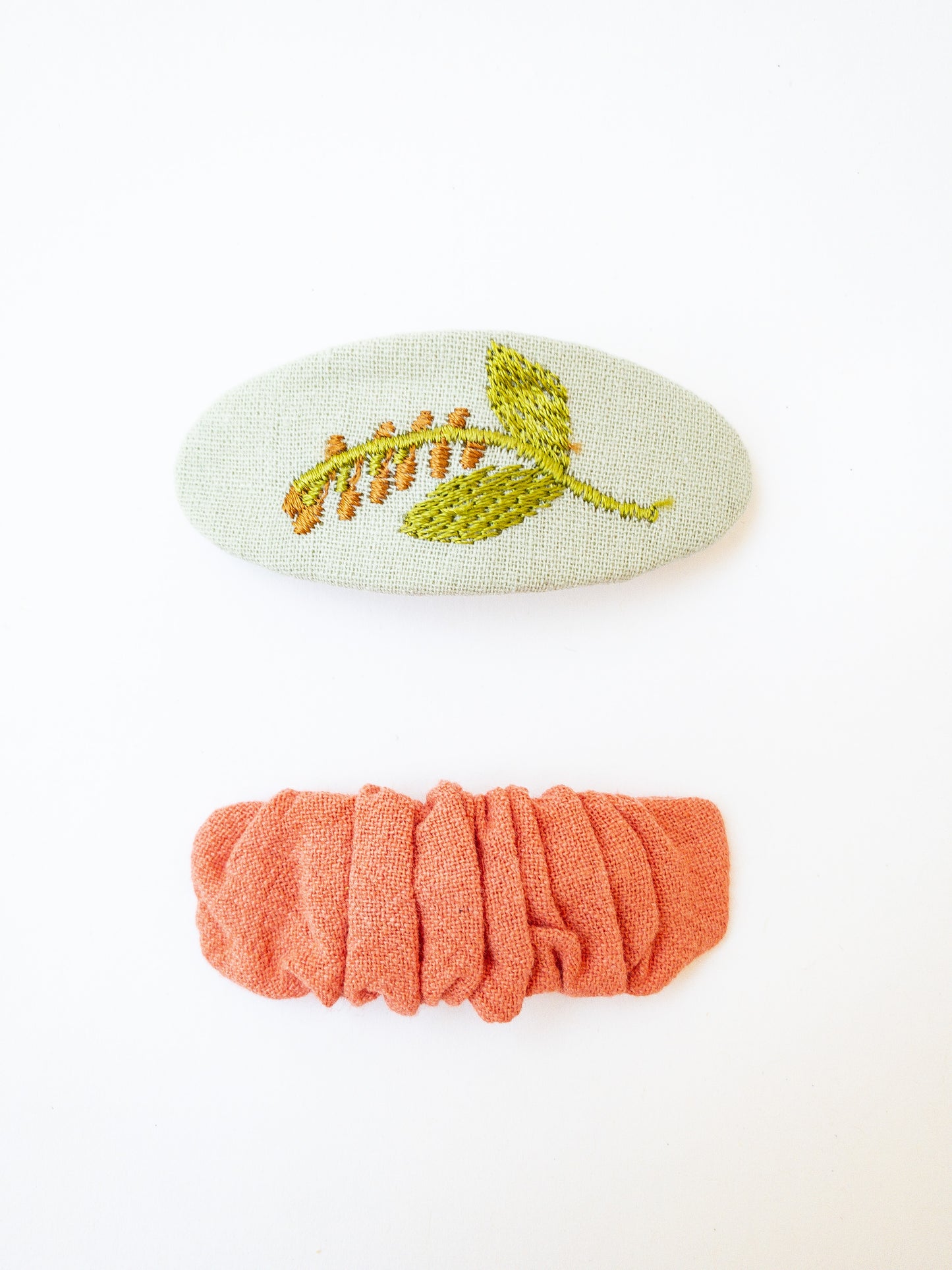 A set of two beautiful fabric wrapped snap clip barrettes. One oval barrette with an embroidered flower and one rectangular ruffled fabric barrette.