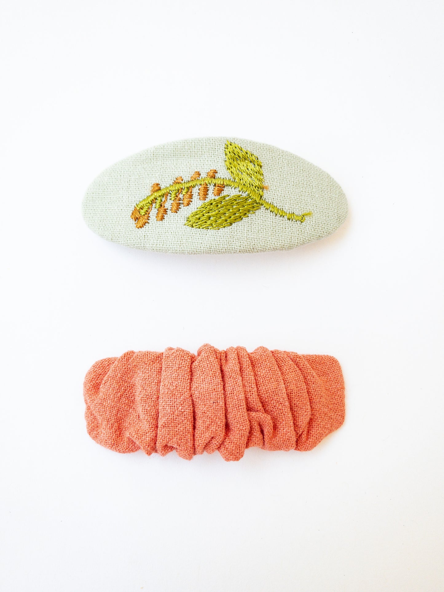 A set of two beautiful fabric wrapped snap clip barrettes. One oval barrette with an embroidered flower and one rectangular ruffled fabric barrette.