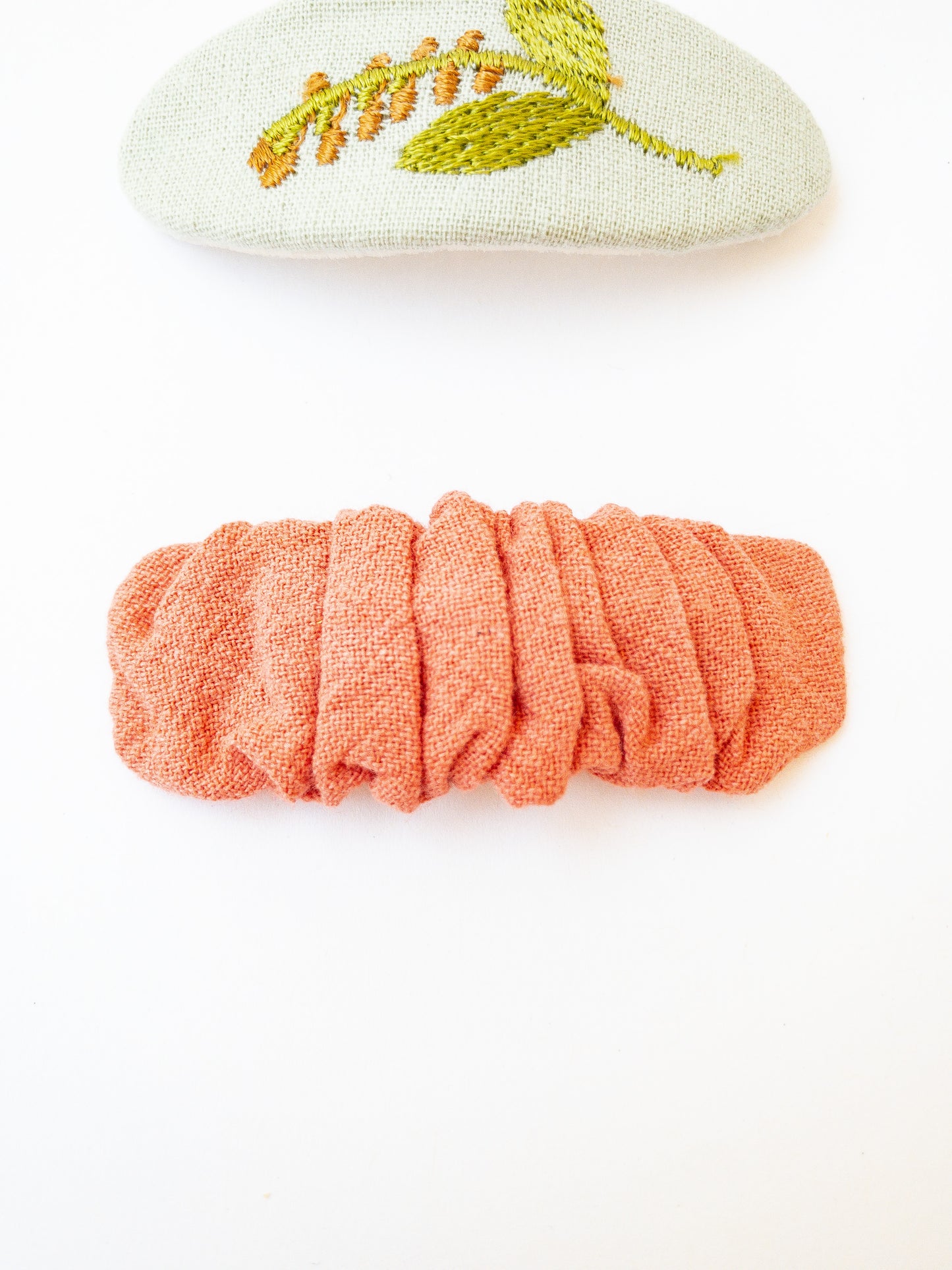 A set of two beautiful fabric wrapped snap clip barrettes. One oval barrette with an embroidered flower and one rectangular ruffled fabric barrette.