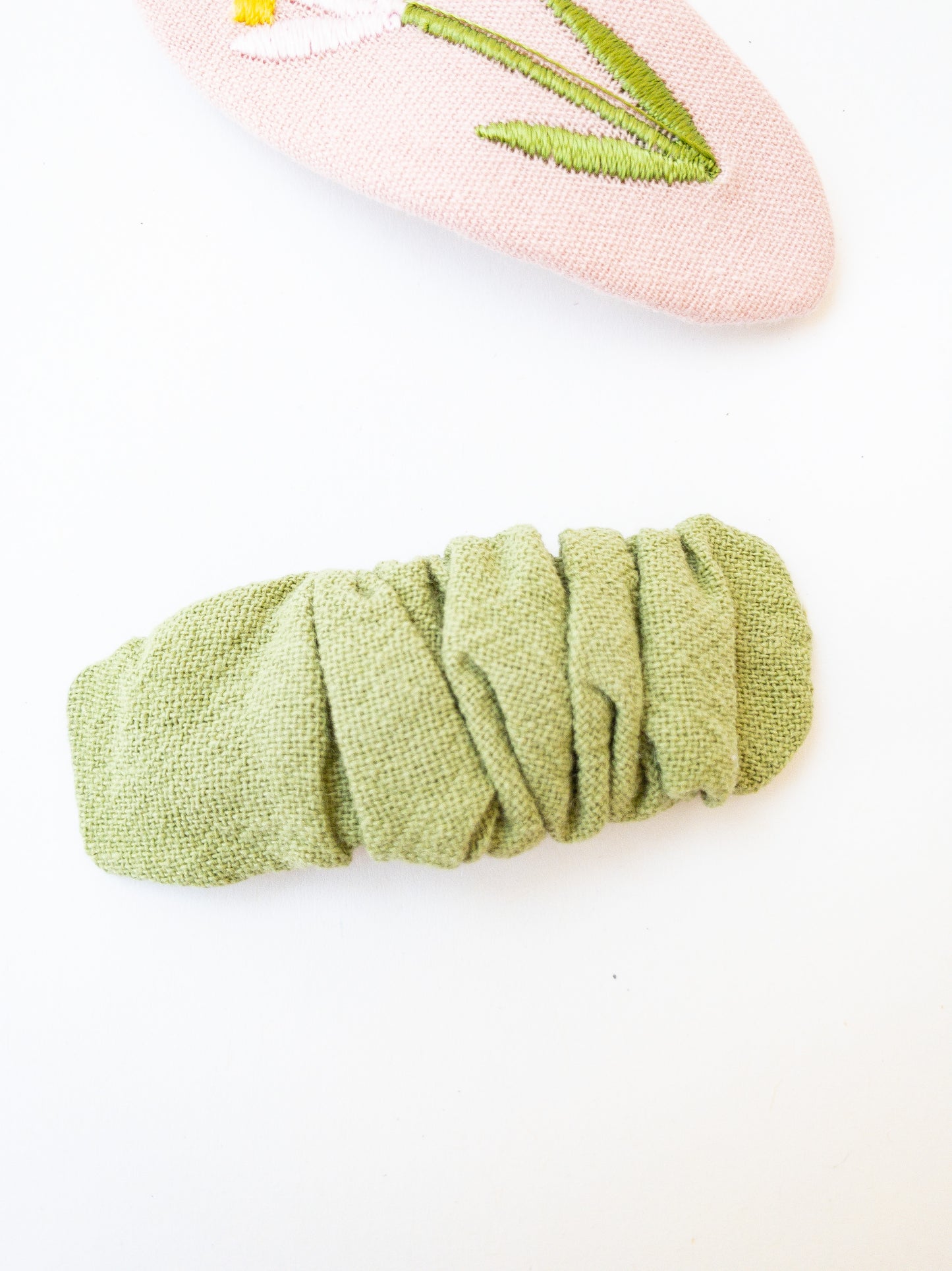 A set of two beautiful fabric wrapped snap clip barrettes. One oval barrette with an embroidered flower and one rectangular ruffled fabric barrette.