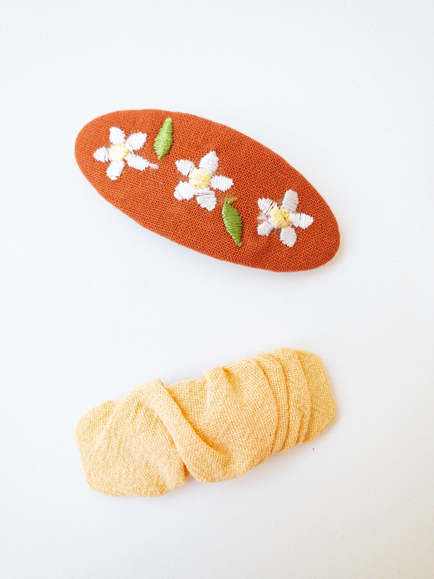 A set of two beautiful fabric wrapped snap clip barrettes. One oval barrette with an embroidered flower and one rectangular ruffled fabric barrette.