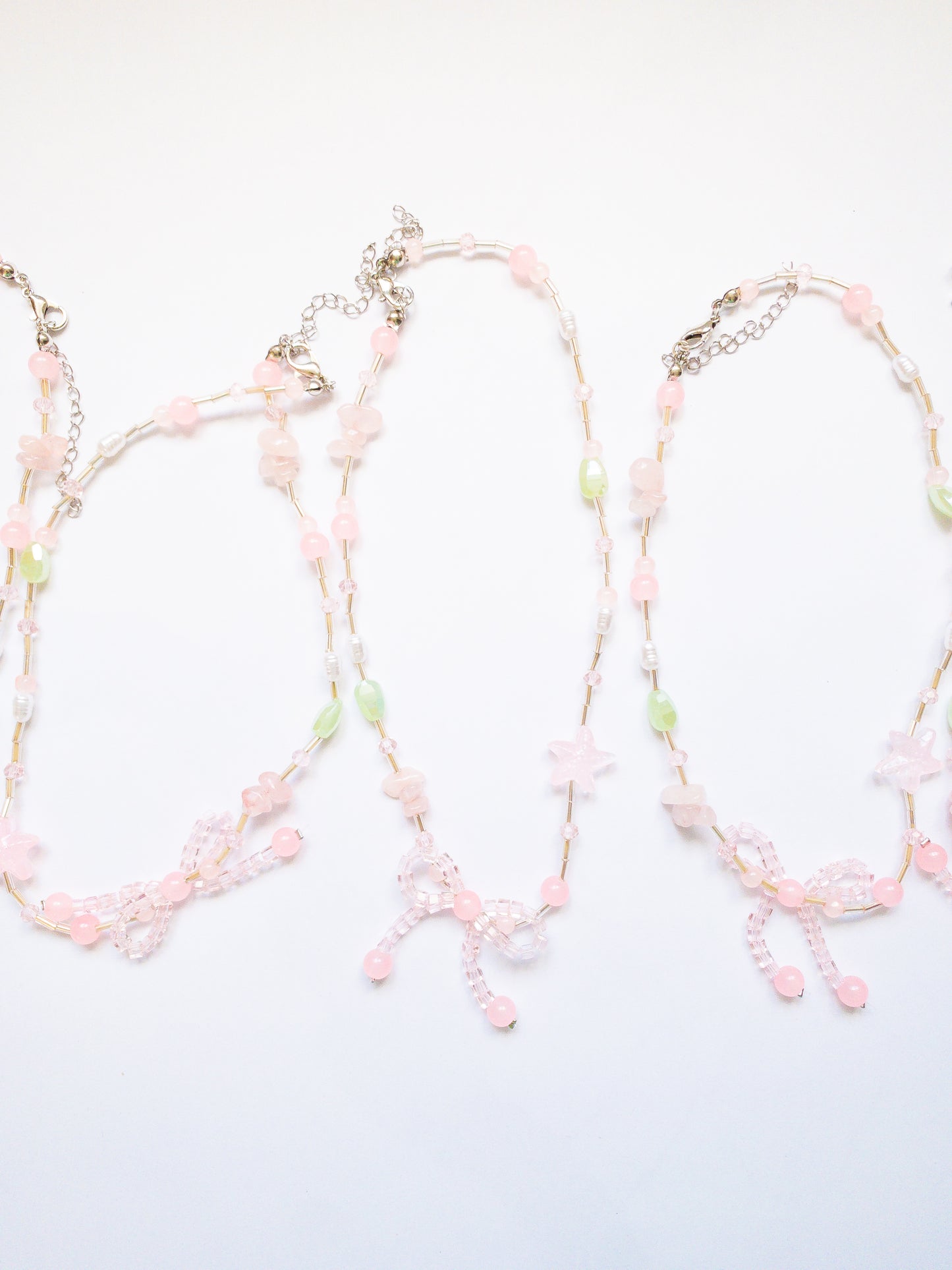 Pretty little beaded bow necklace with light pink and green stones, pearls, and a pink starfish. A subtle and delicate way to add bows to your look.