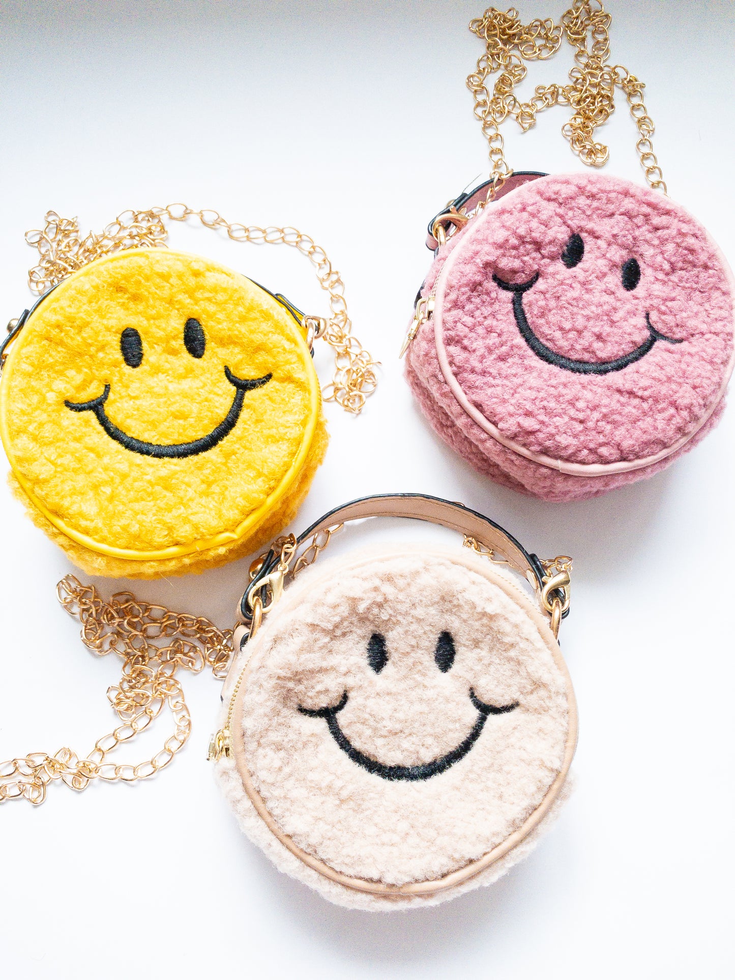 The cutest smiley face bag! This little purse is fuzzy and happy with a single zip open. It has a small open pocket in the back and a short vegan leather handle. The gold chain strap is removable. Choose from 3 cute colors.