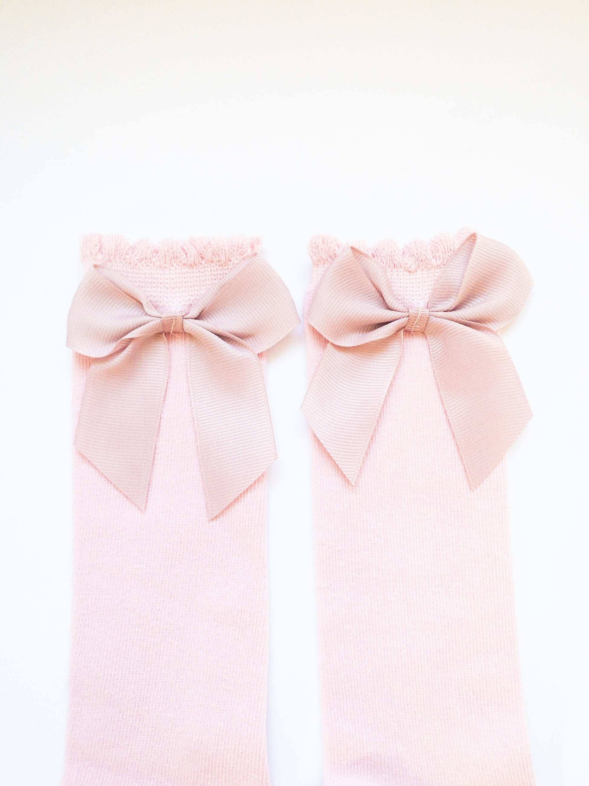 A sweet pair of kids knee high socks in a pretty pink with a dusty pink bow on each sock. The ruffled detail makes the socks even sweeter.