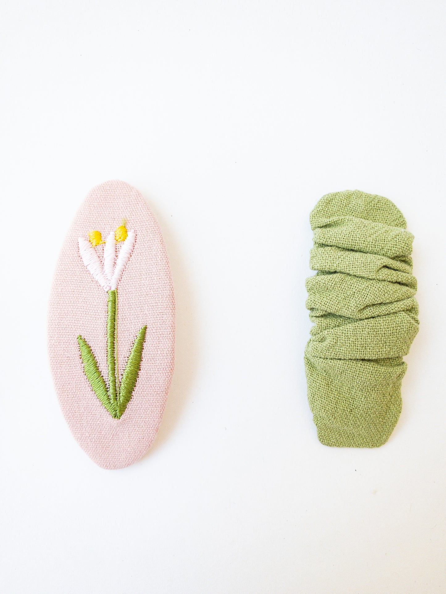 A set of two beautiful fabric wrapped snap clip barrettes. One oval barrette with an embroidered flower and one rectangular ruffled fabric barrette. 