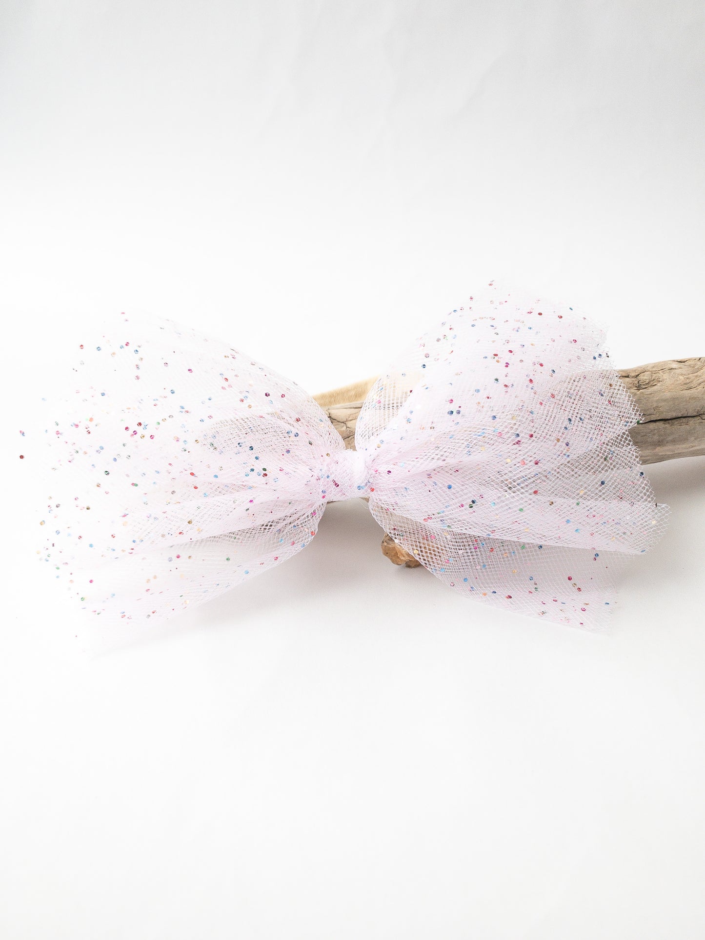 A large pretty in pink bow covered in colorful flecks of glitter! The glitter and mesh details of this bow make it so fun and festive and perfect for your little one.  Great for kids with little to no hair. The nylon elastic is super stretchy and super soft.
