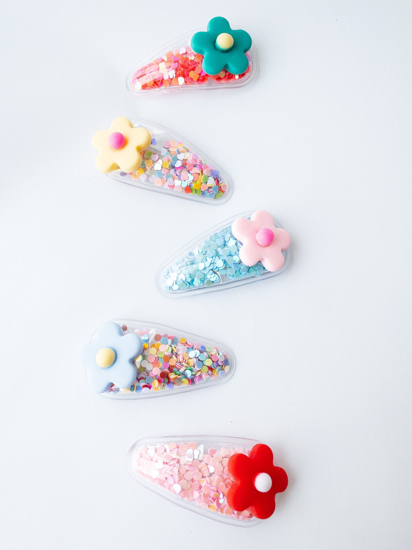 Our signature shaker hair clips but with flowers! Each snap clip is a triangular pouch filled with the most fun confetti--hearts and circles. And to top it all off, there is a pretty flower on the end of each clip. These are sure to make anyone smile!