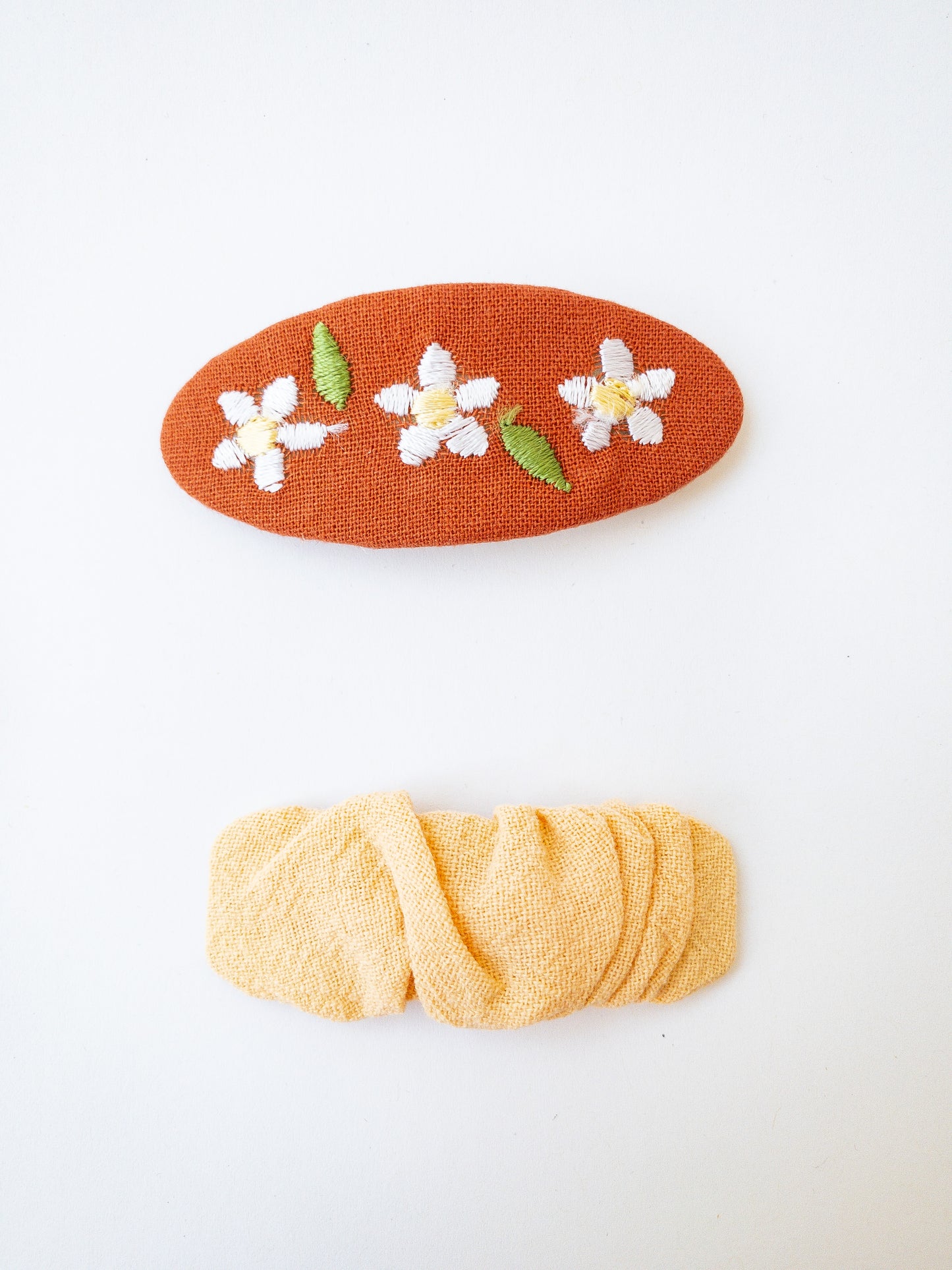 A set of two beautiful fabric wrapped snap clip barrettes. One oval barrette with an embroidered flower and one rectangular ruffled fabric barrette. 