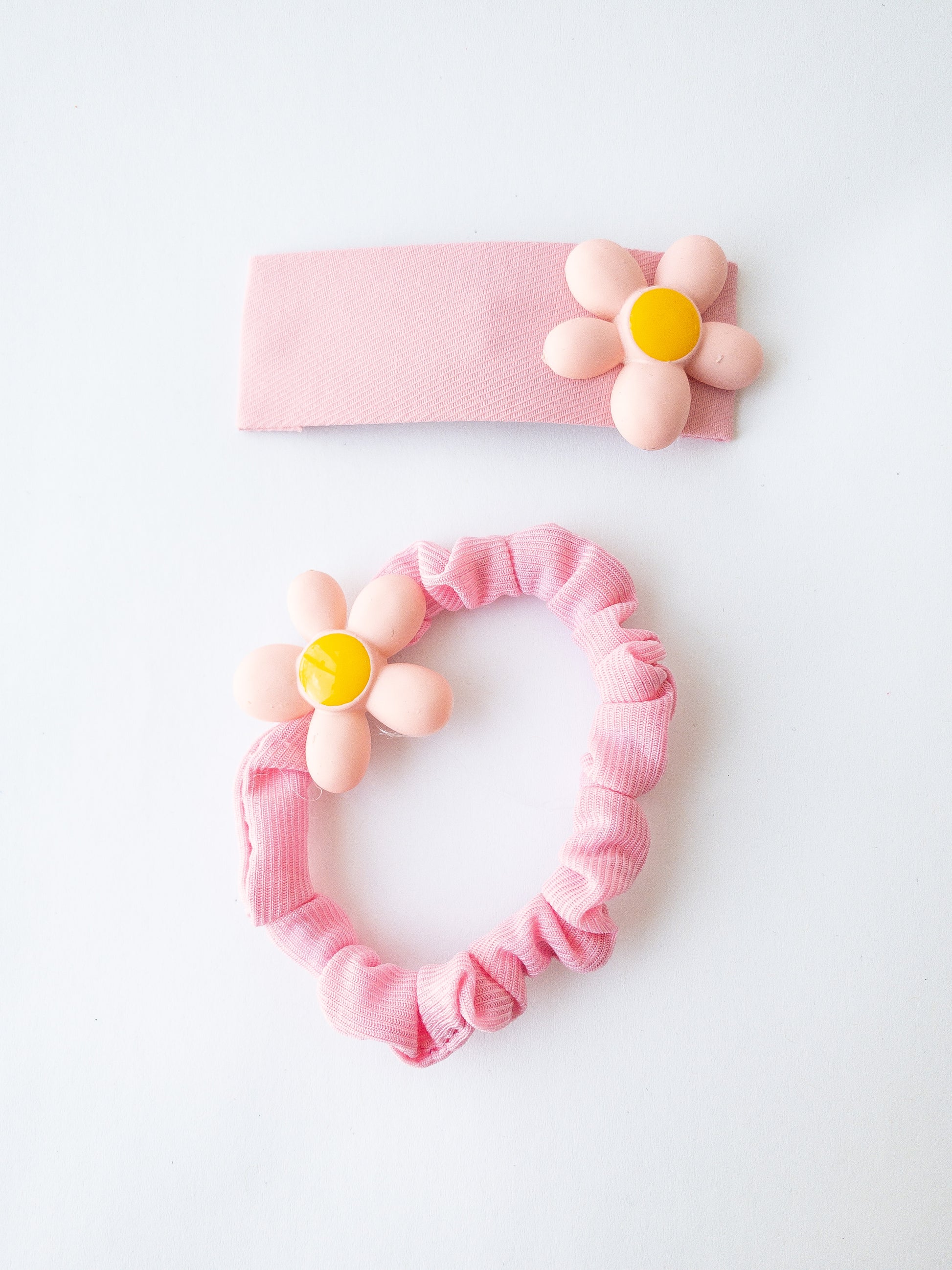 A soft, thin fabric wrapped scrunchie with a single pretty flower and a fabric wrapped rectangle snap clip with a matching flower in this duo set. Comes in 4 bright and sunny colors. 