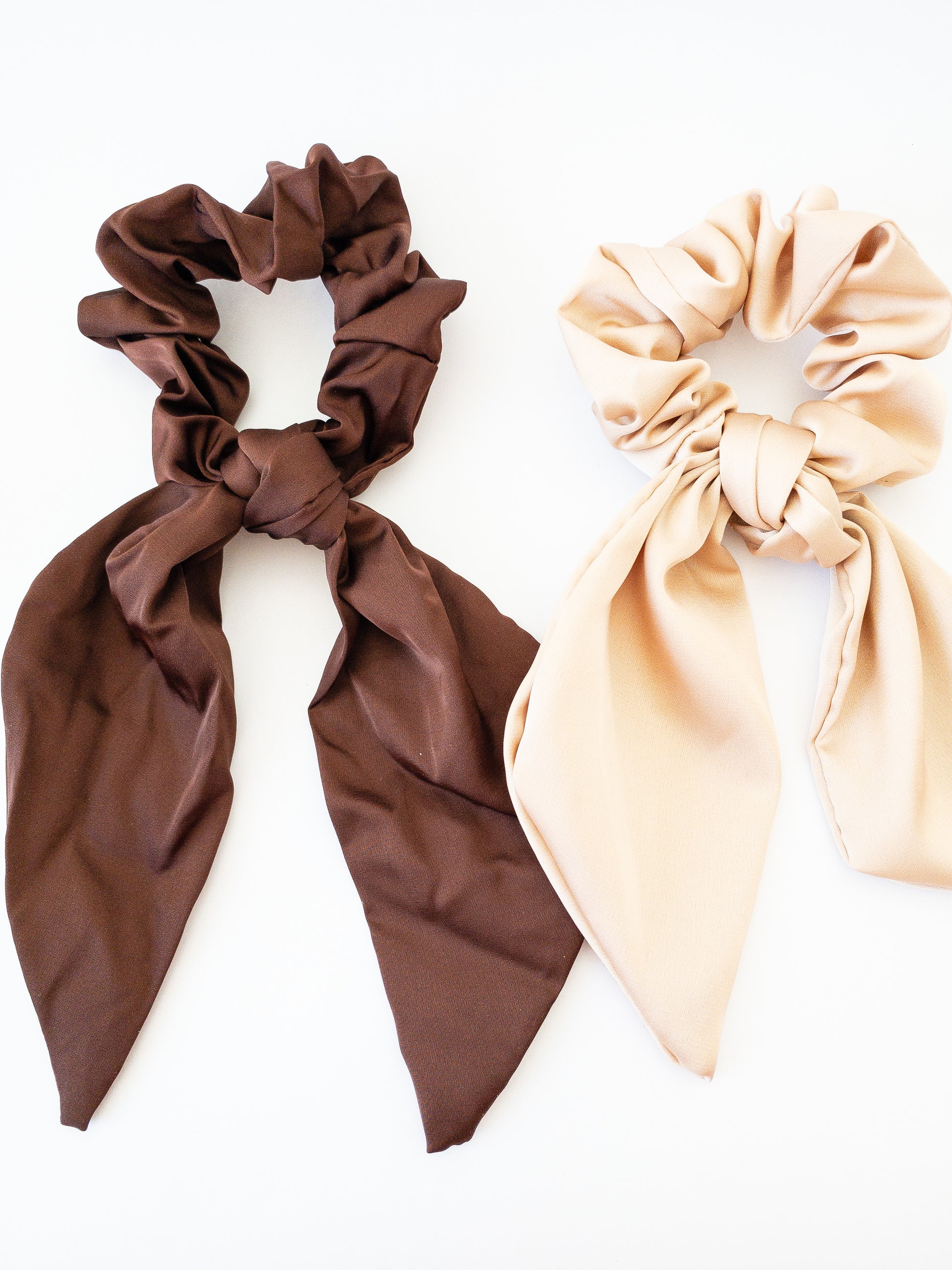 Two silky soft scrunchies each with a classic tied bow. These come in a set of two: one beige and one brown. Classic colors great for everyday wear such as a low ponytail.