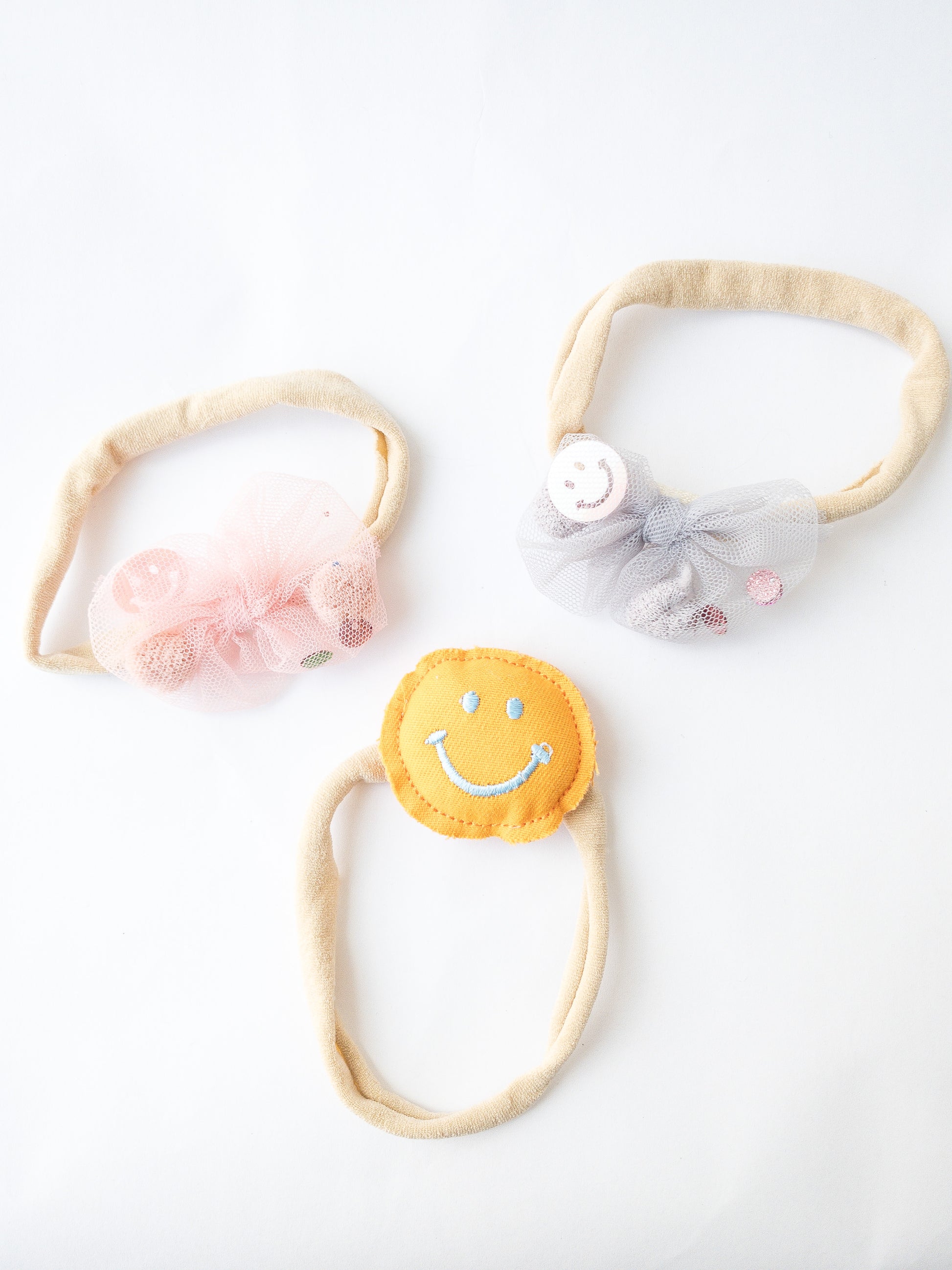 A 3-piece set. This set comes with a friendly plush smiley face headband, a pink mesh bow headband and a grey mesh bow headband with pom poms, sequins and smiley faces inside. Great for kids with little to no hair. The nylon elastic is super stretchy and super soft.