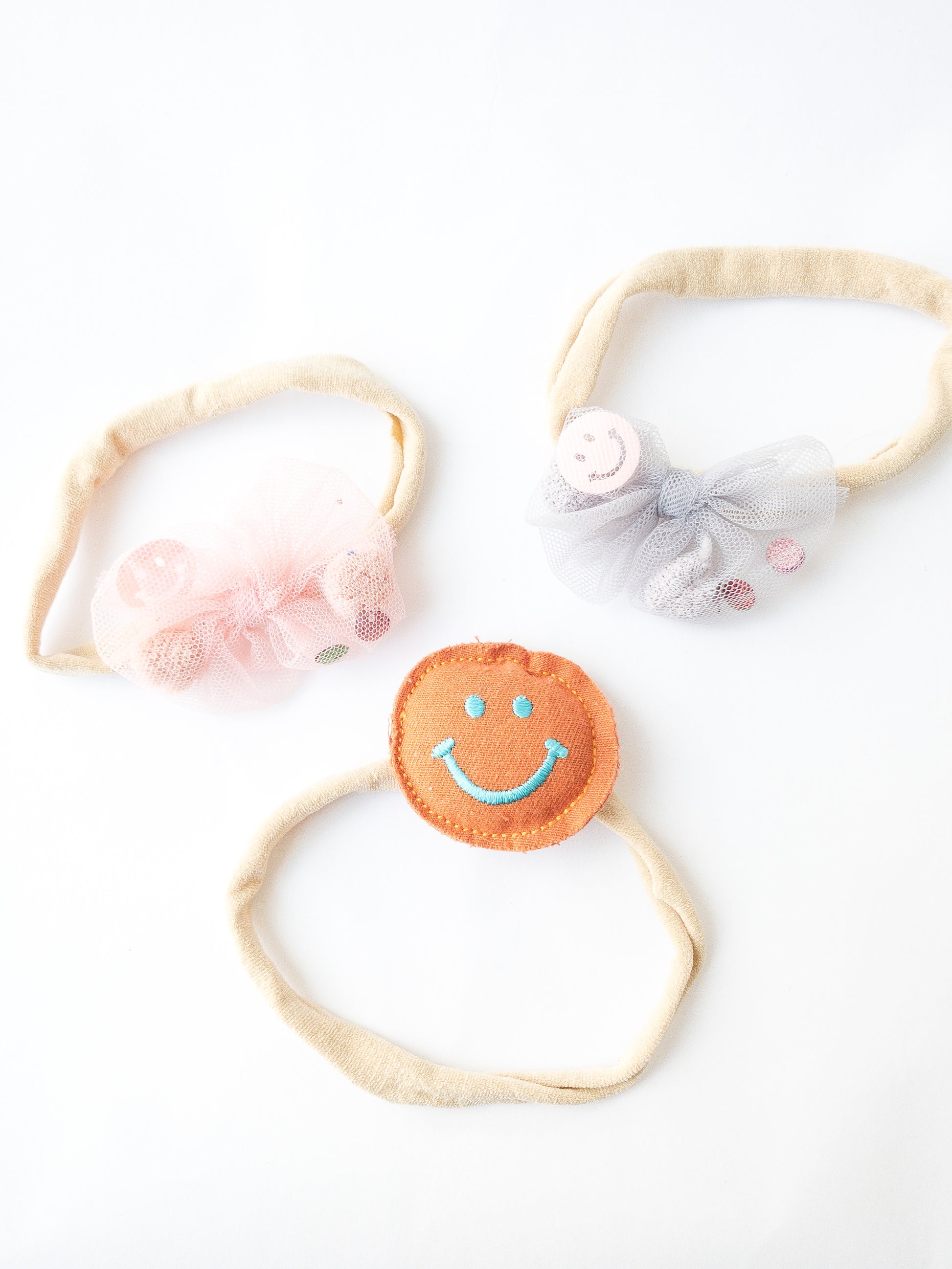 A 3-piece set. This set comes with a friendly plush smiley face headband, a pink mesh bow headband and a grey mesh bow headband with pom poms, sequins and smiley faces inside. Great for kids with little to no hair. The nylon elastic is super stretchy and super soft.