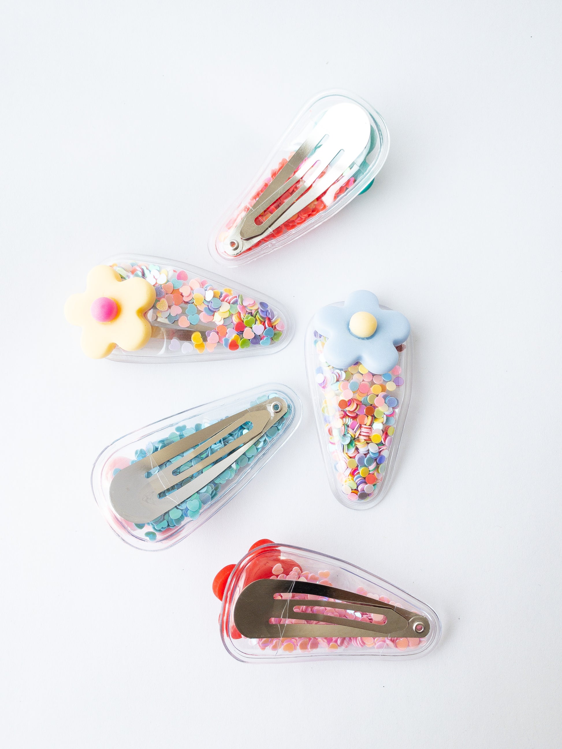 Our signature shaker hair clips but with flowers! Each snap clip is a triangular pouch filled with the most fun confetti--hearts and circles. And to top it all off, there is a pretty flower on the end of each clip. These are sure to make anyone smile!